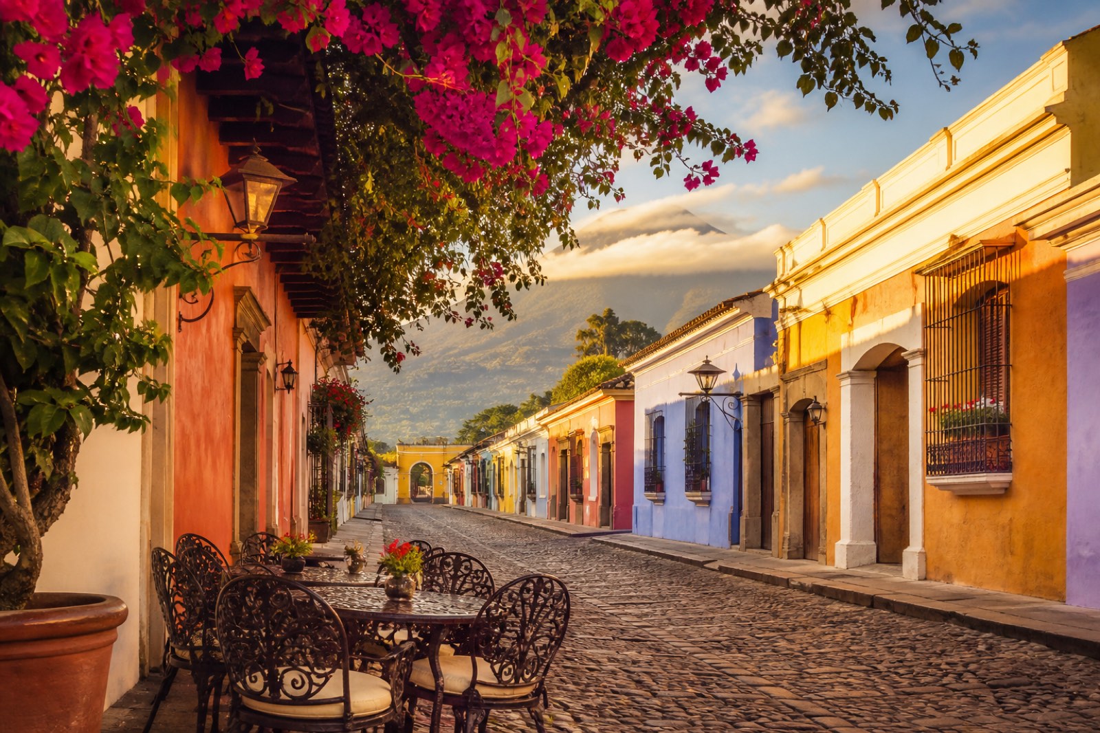 Colonial street in Antigua Guatemala with vibrant bougainvillea, cobblestones, and the Volcán de Agua rising behind colorful historic buildings