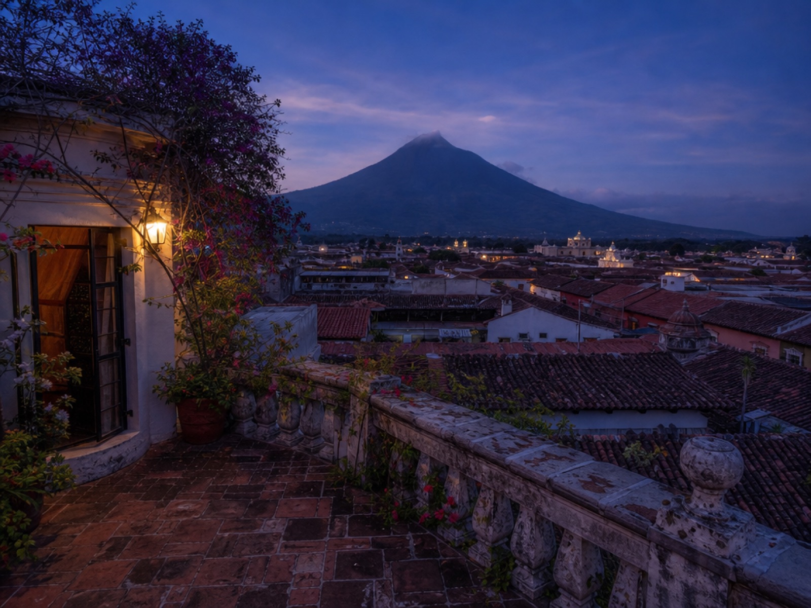 Colonial roof terrace in Antigua Guatemala at dusk with terracotta tile rooftops and the Volcan de Agua silhouette