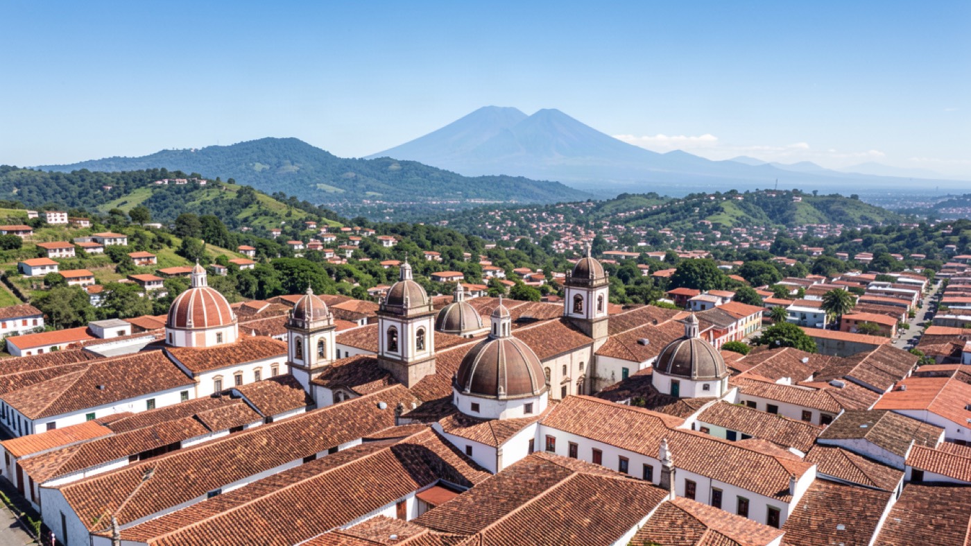 Vista panorámica de la Antigua Guatemala colonial con cúpulas de iglesia, techos de teja y el volcán a lo lejos