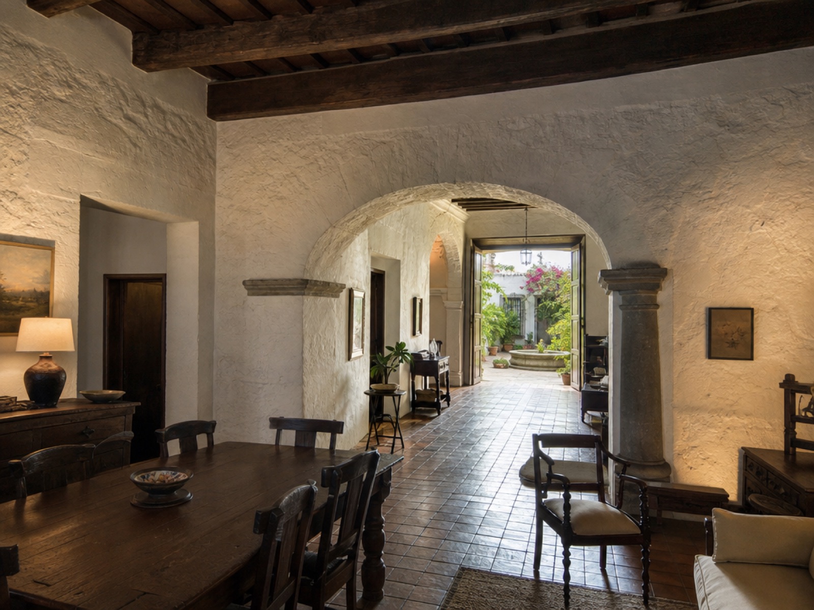 Interior of a restored colonial home in Antigua Guatemala with thick stone walls, exposed wooden beams and an arched doorway opening onto a courtyard
