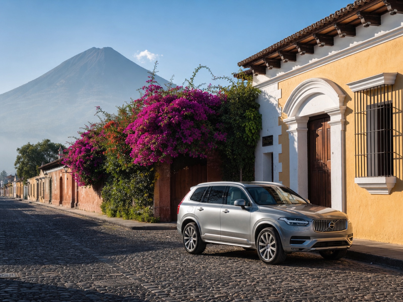 Silver SUV parked on a cobblestone street beside a colonial building with bougainvillea in Antigua Guatemala, Volcán de Agua in the background
