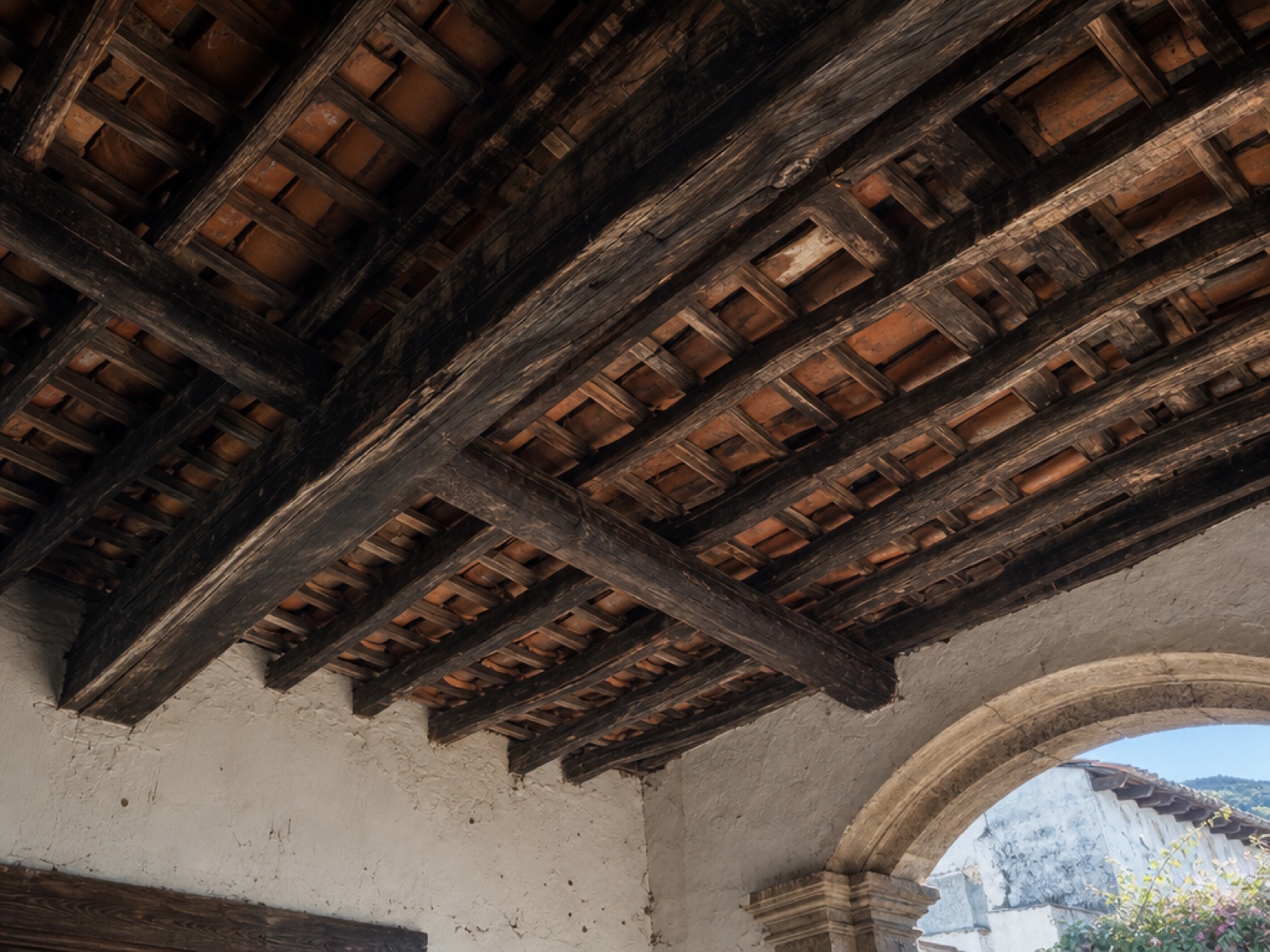 Underside of a colonial roof in Antigua Guatemala showing aged wooden beams and rafters supporting terracotta clay tiles in bright midday light