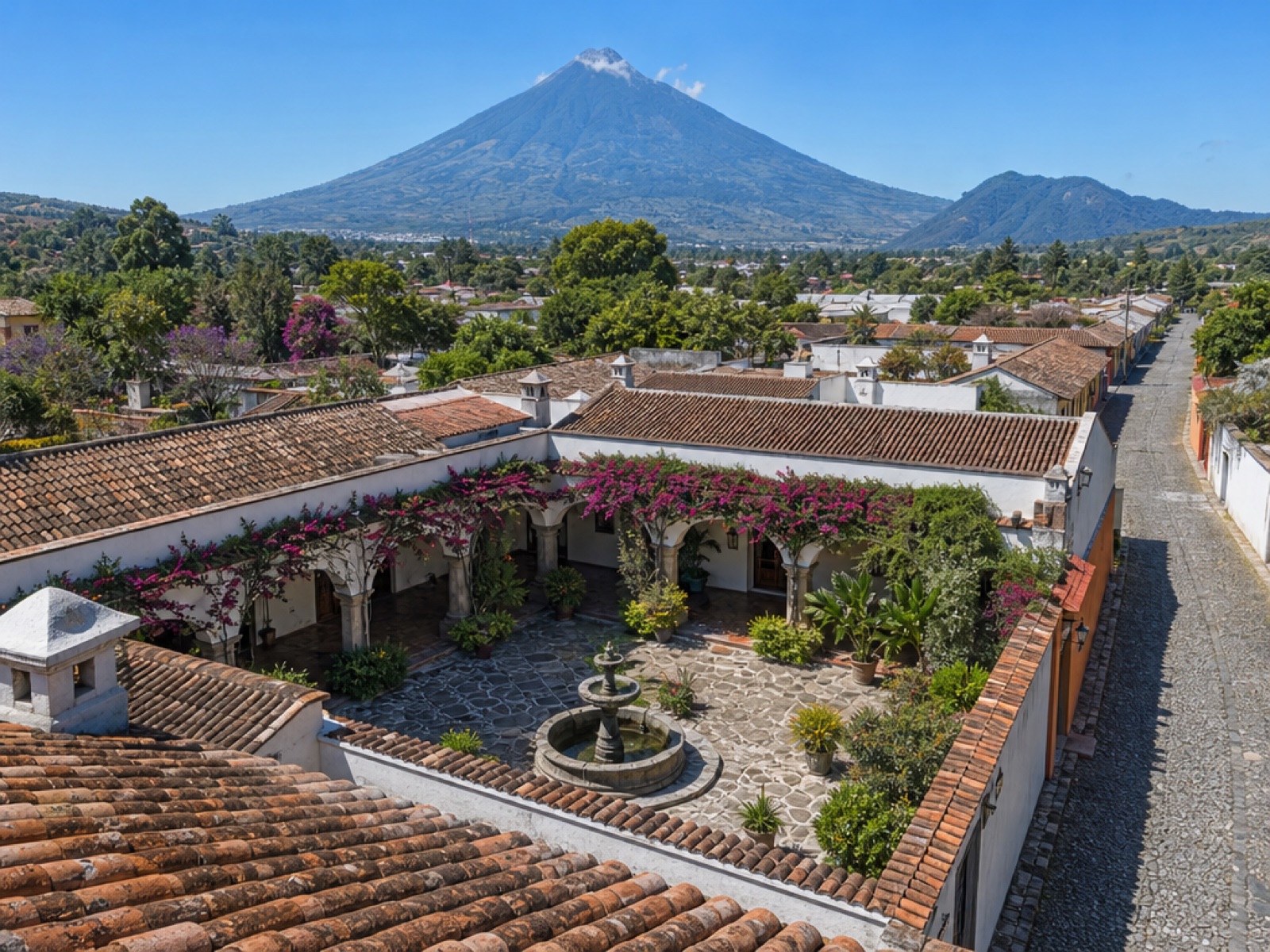 Elevated view of a colonial Antigua Guatemala property with a central courtyard fountain, terracotta roofs and Volcán de Agua