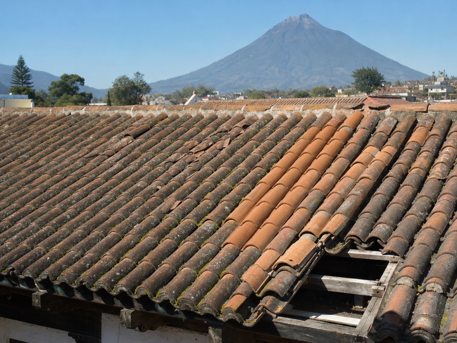 Weathered terracotta clay tile roof of a colonial house in Antigua Guatemala with new tiles and Volcán de Agua in the background
